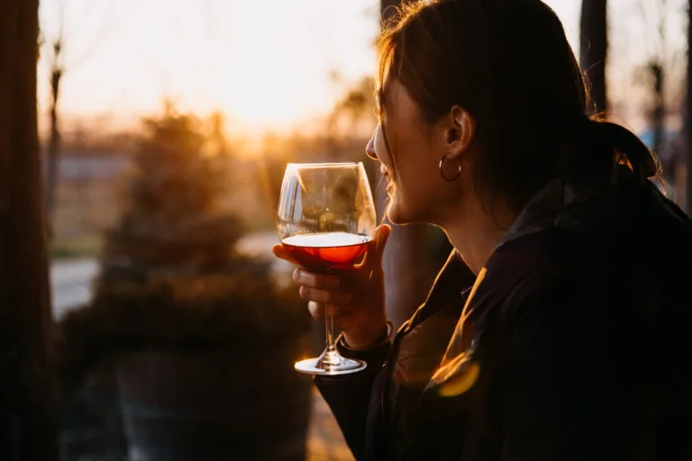 Jovem mulher segurando uma taça de vinho tinto.